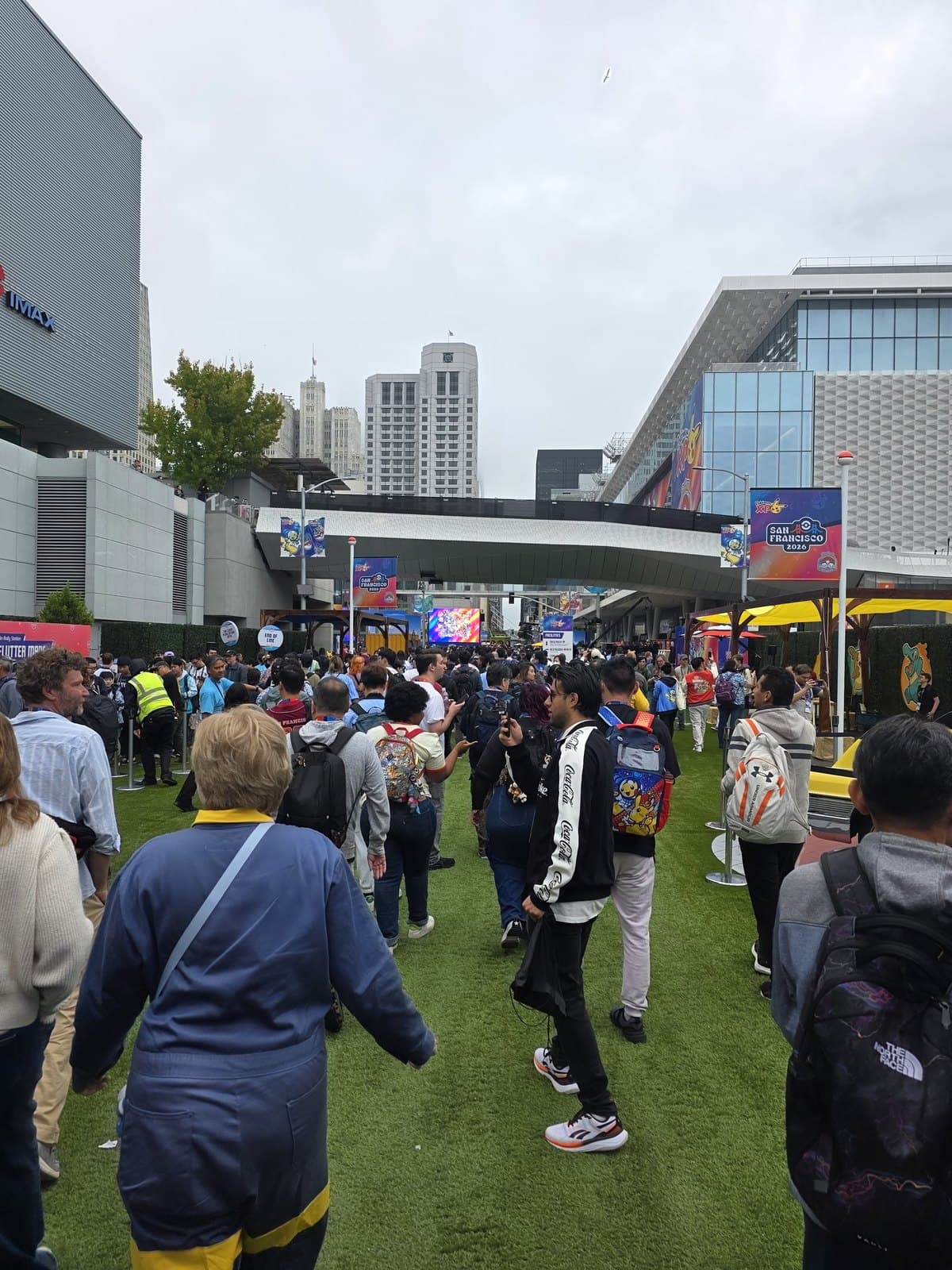 Crowds of people walking across grass towards the convention centre on a grey morning