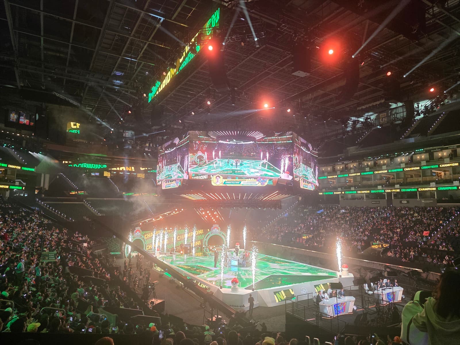 A wide view of the arena from high in the stands, the floor lit green with the crowd filling the tiers