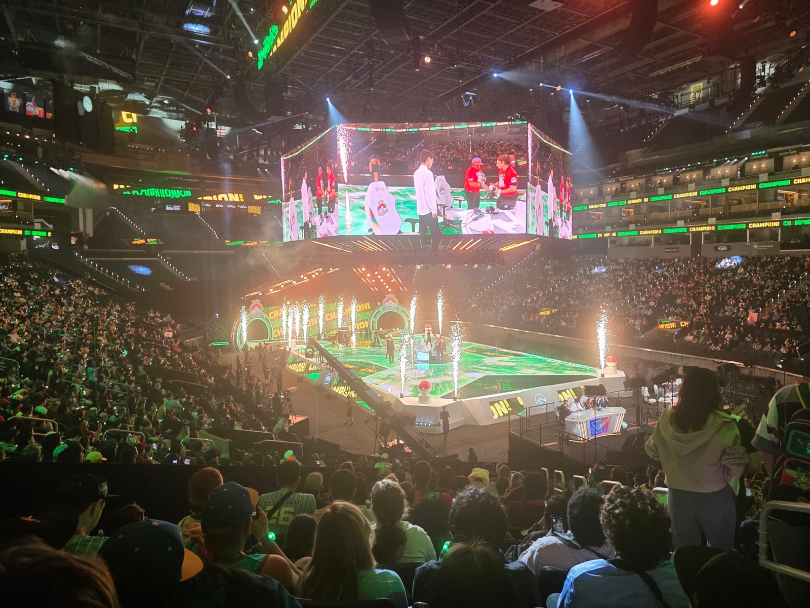 The arena floor lit in green and pink with the stage in the centre and a full crowd around it