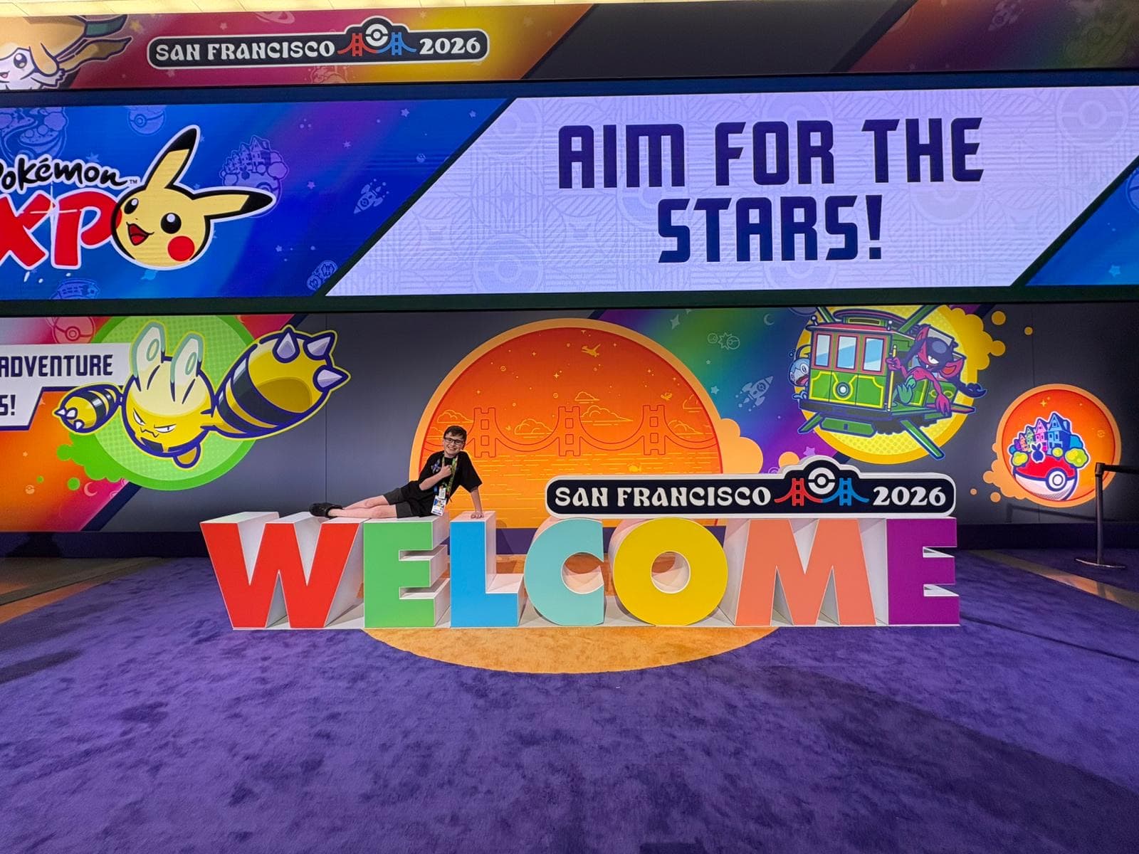 A large stage with WELCOME in giant letters, a Pikachu banner and screens reading Aim For The Stars